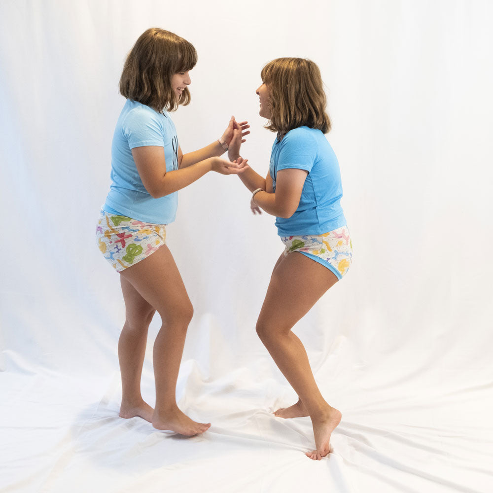 two twin girls dancing on a white backdrop while modeling wunderundies underwear