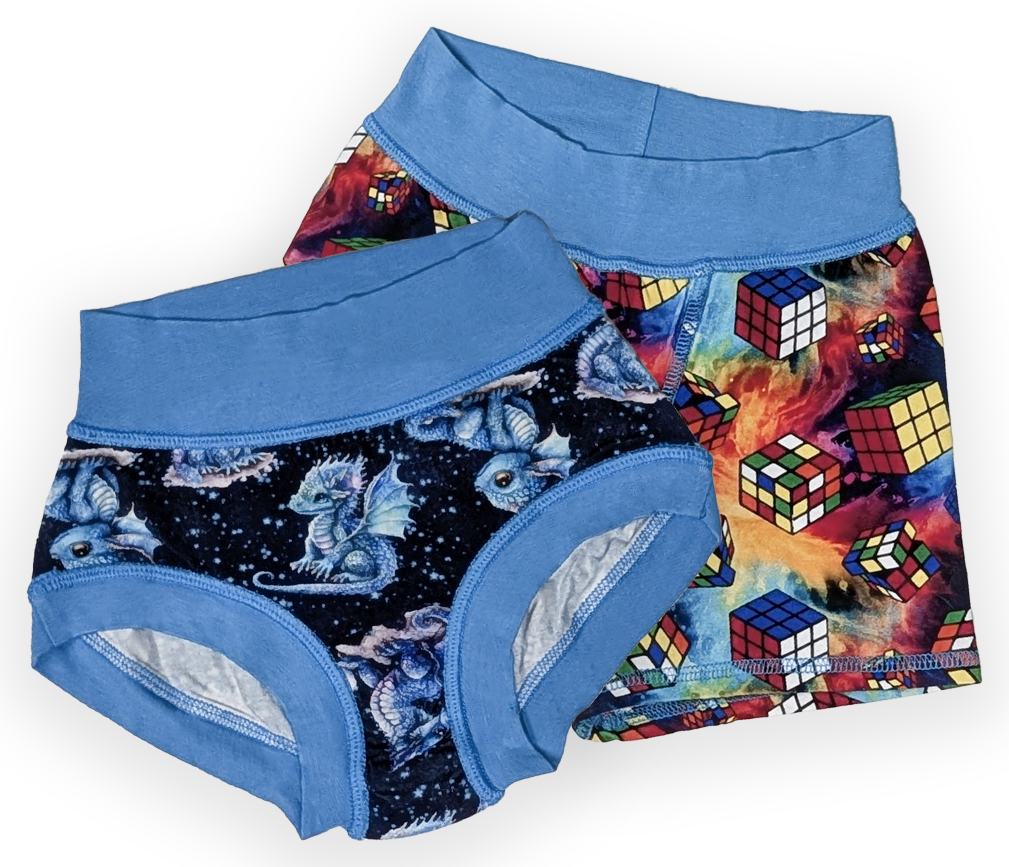 Two pairs of children's sensory friendly underwear laid flat on a white background. The front pair is a brief style and has a blue waistband and leg openings with a dark navy print of blue dragons on a starry background. The back pair is boxer style and features rubiks cubes with a blue waistband.