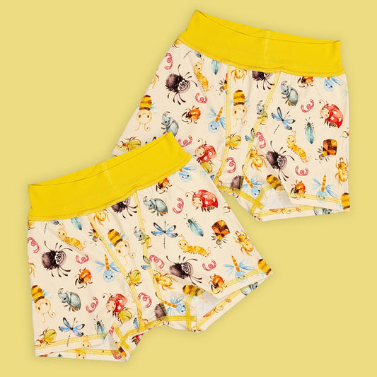 two pairs of flat seamed boxer shorts that have yellow waistbands and a cute bug print