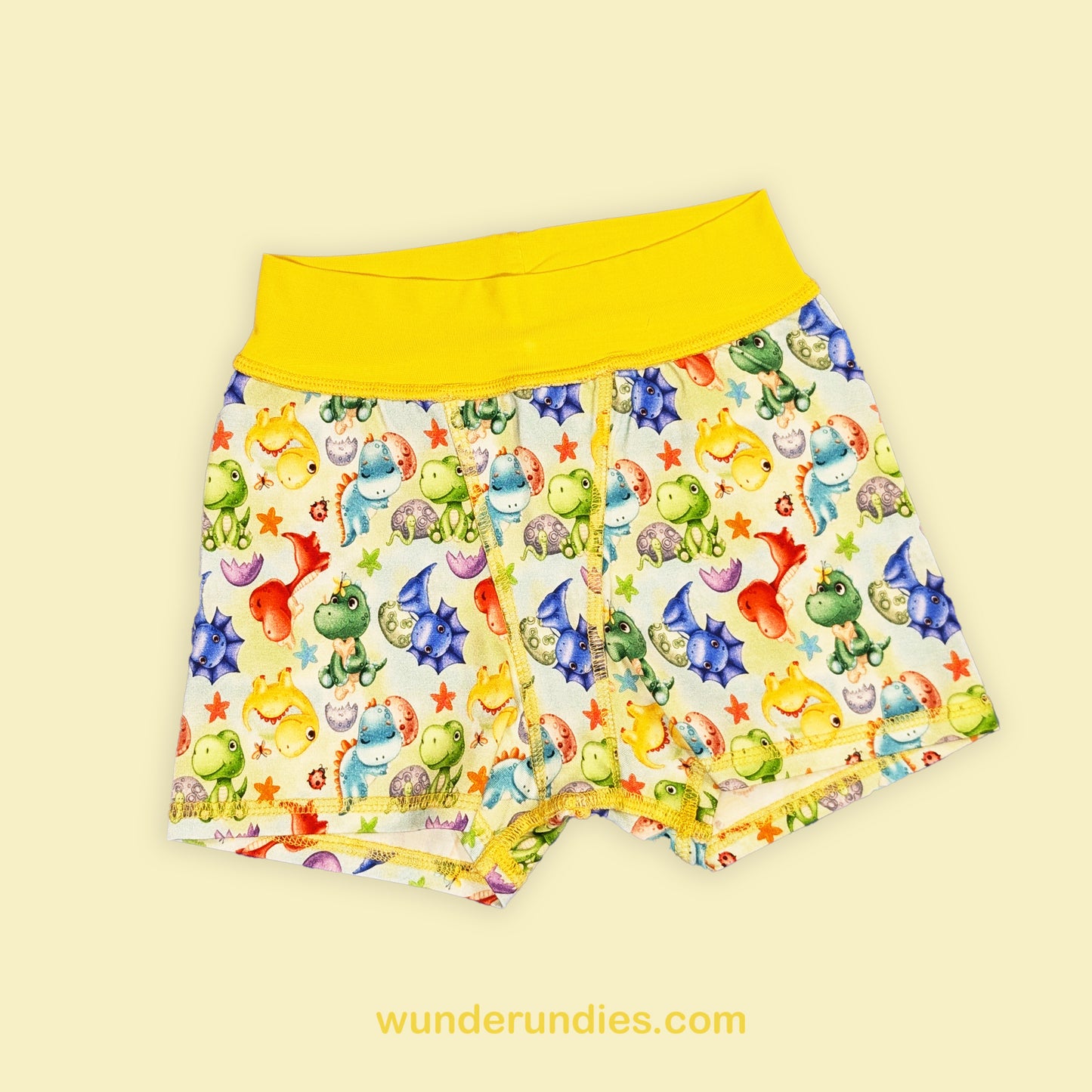 Colorful children's boxer shorts with a dinosaur pattern on a light yellow background